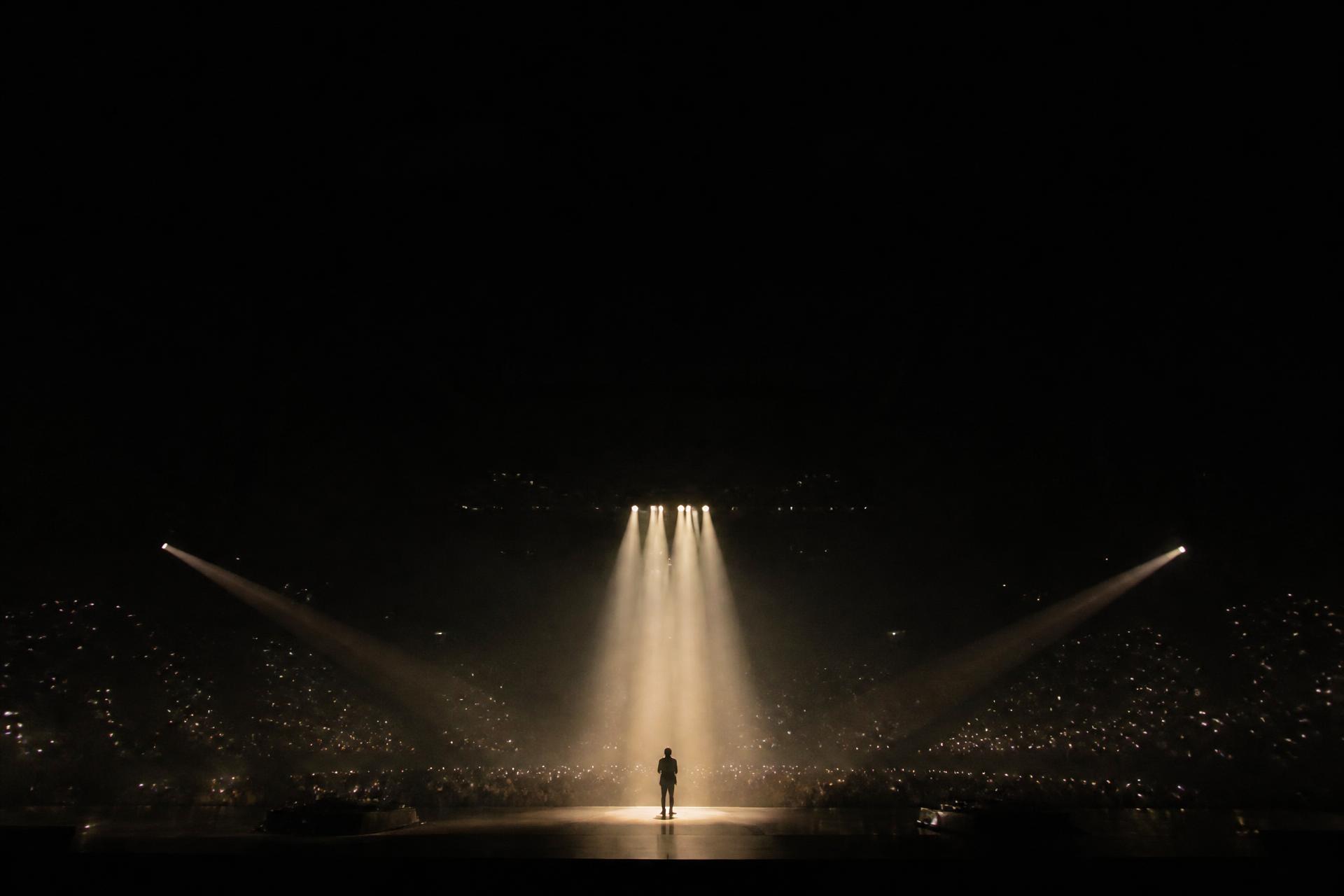 A performer under stage lighting in a darkened concert hall